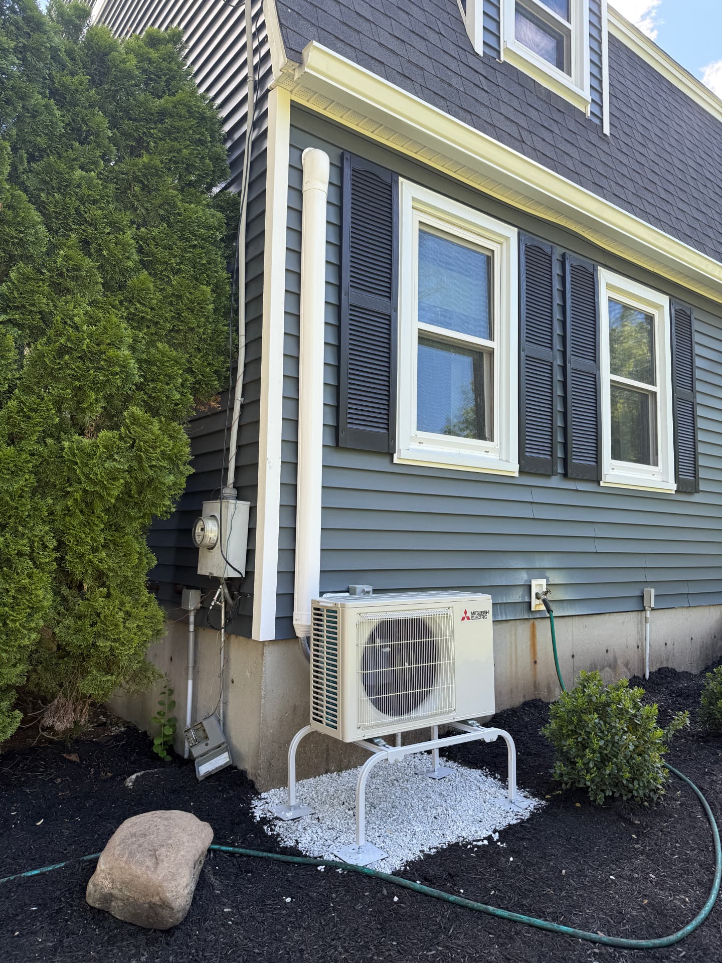 Mitsubishi condenser on a raised stand over white stone in a mulched bed