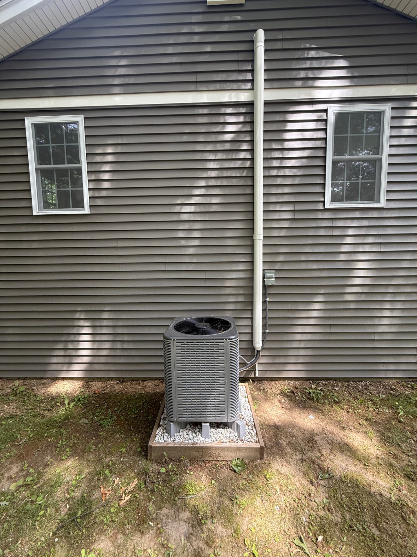 Central air condenser set on a stone pad with clean line run up the siding